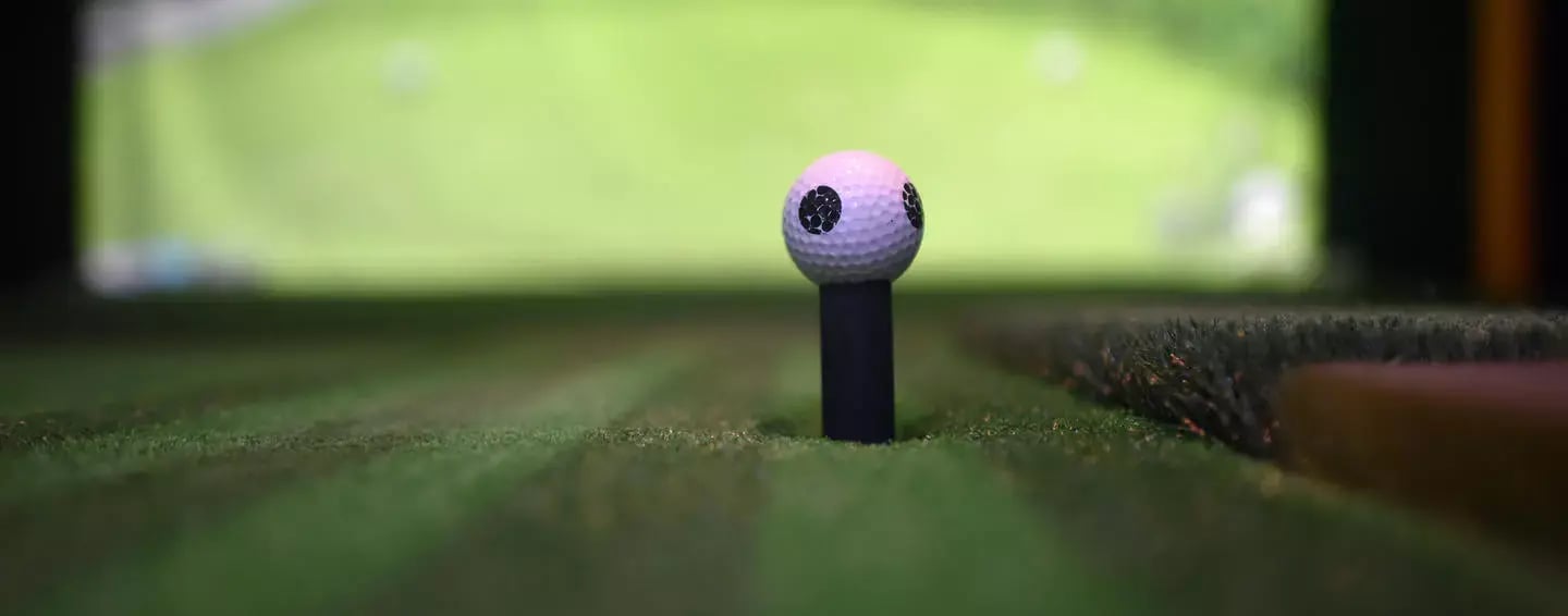 Golf ball on a tee in front of golf course projected on screen