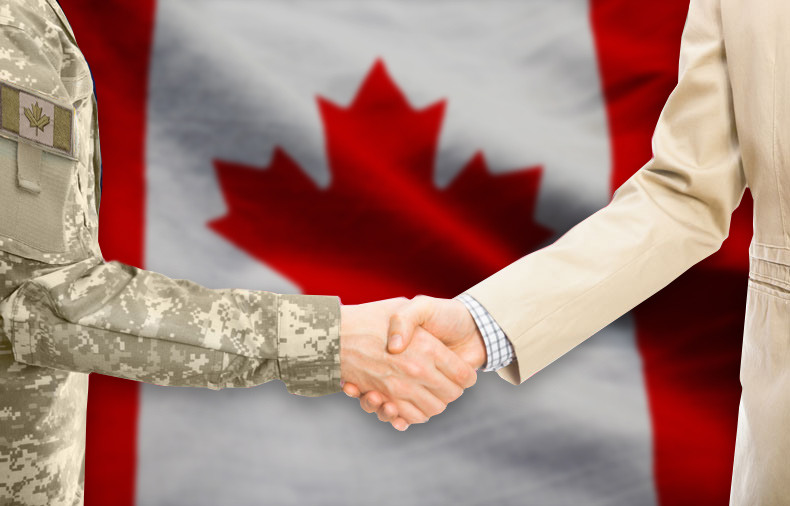A man with business suit and another man with army uniform shaking hands in front of Canadian flag