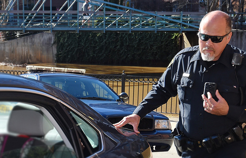 Police officer leaning on car while pressing on talk button on his radio