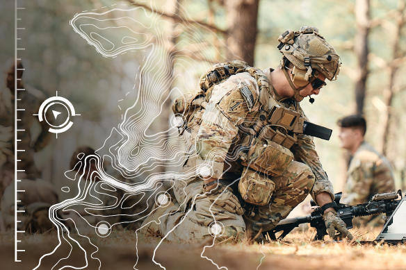 Soldier pointing down at map on the ground while kneeling.