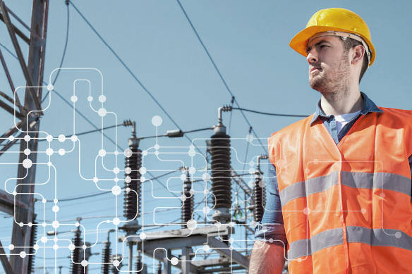 Man with safety hat and vest posing with powerlines in the background